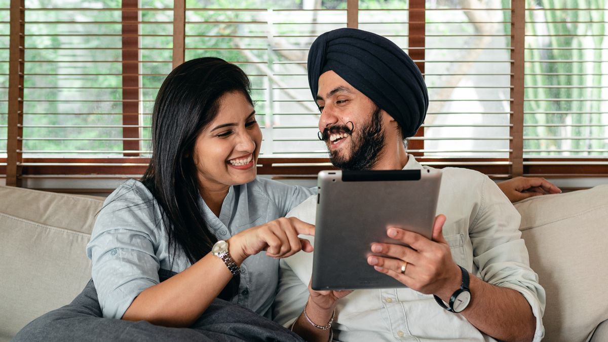 Indian couple laughing on a sofa while browsing sex toys for couples on a tablet